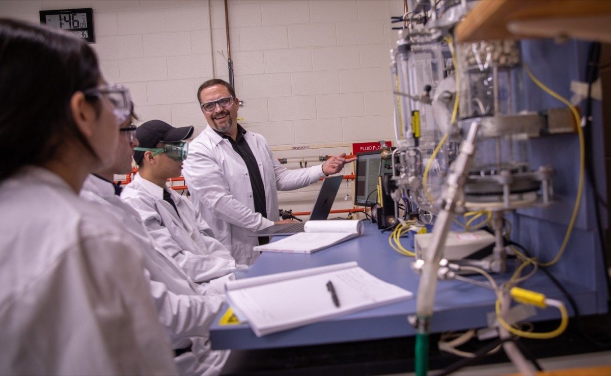 An instructor demonstrates chemical engineering equipment to students in a teaching laboratory.