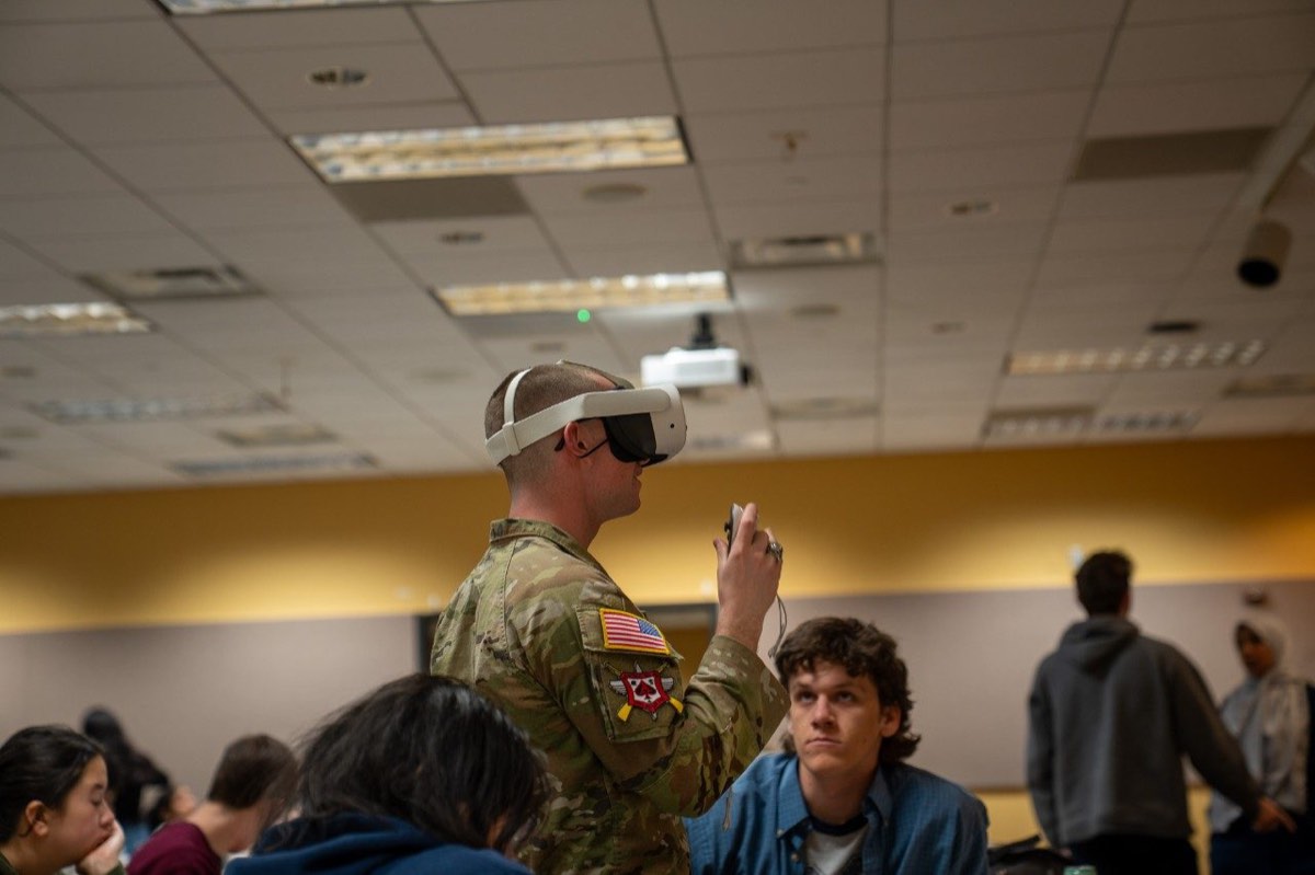 A uniformed participant uses a virtual-reality headset as students observe in a classroom.