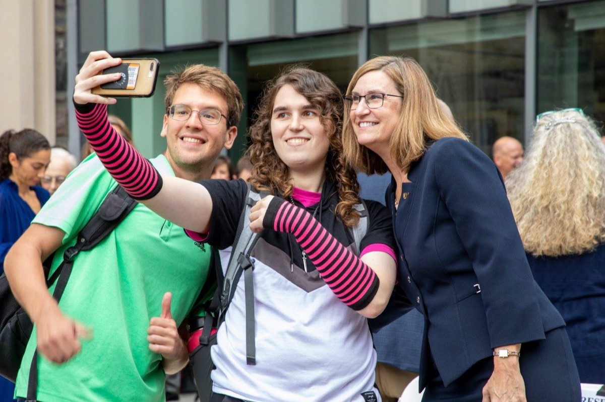 Two students take a selfie with a college dean during a campus gathering.