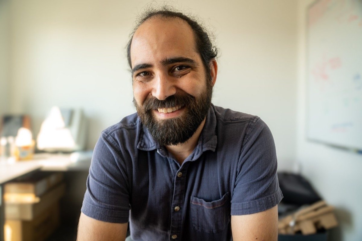 A bearded faculty member smiles in a softly lit office portrait.