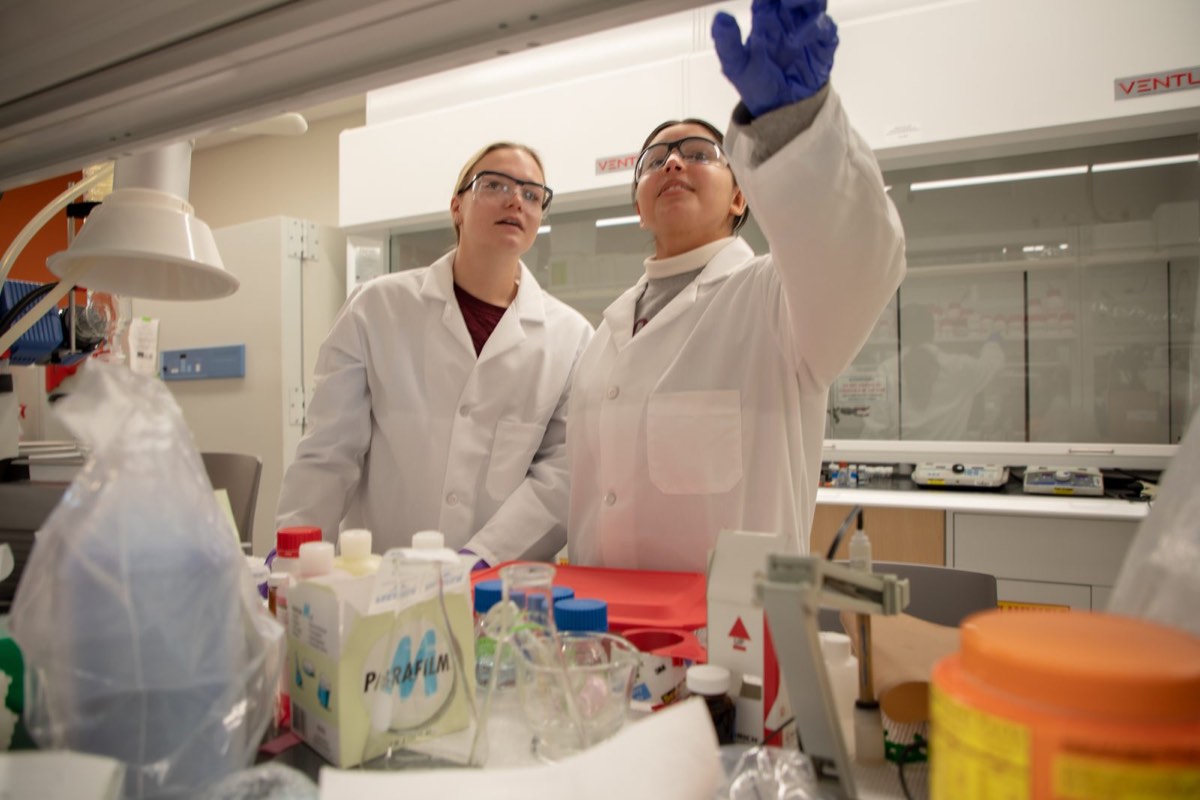 Two researchers in protective eyewear work together at a laboratory bench.