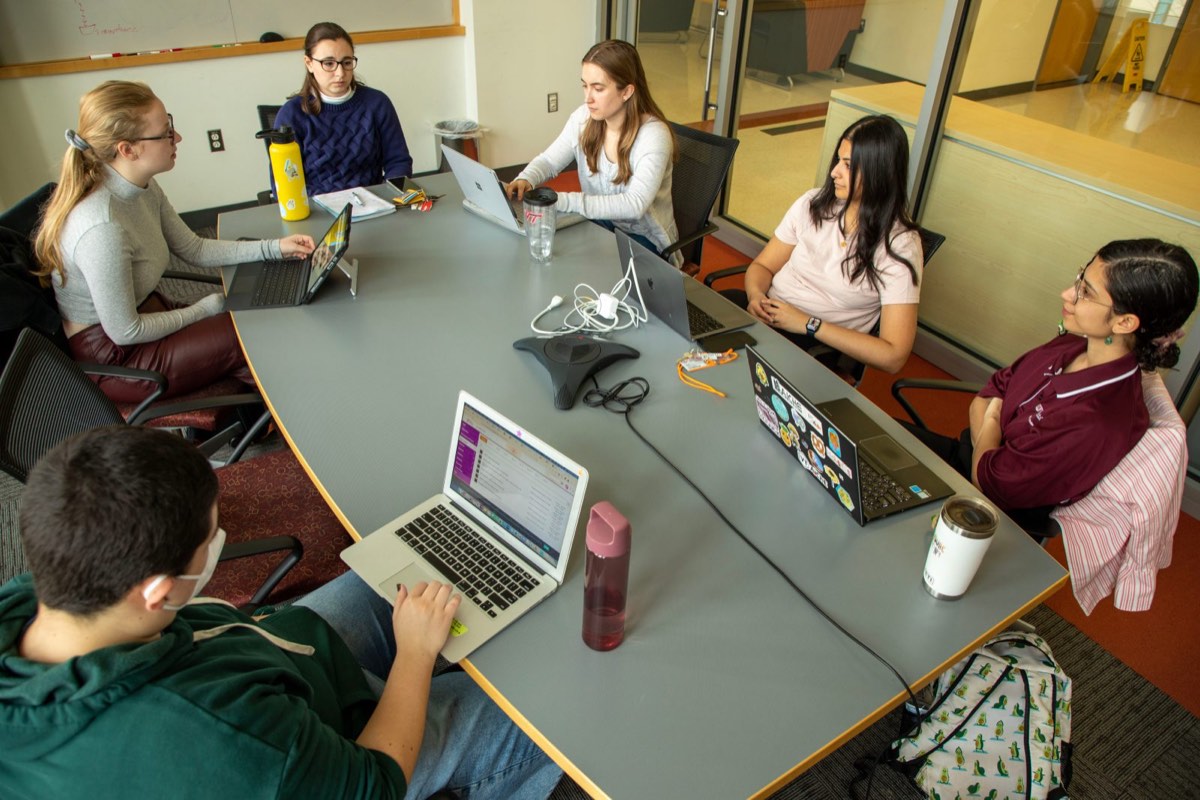 Students with laptops gather around a conference table for an organization meeting.